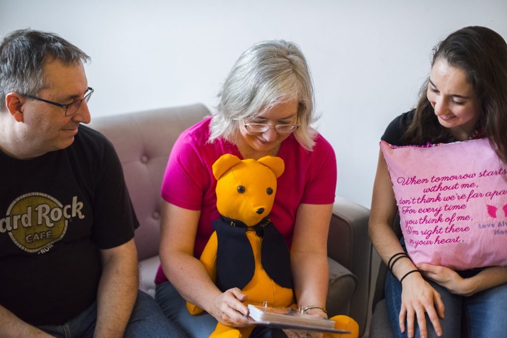 Anne and her family cherishing their memorial bear and pillow while looking at old photos.