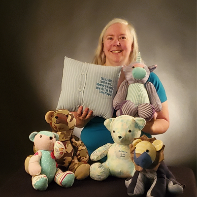 Anne holding a selection of memory bears and a pillow she created from the clothes of lost loved ones.
